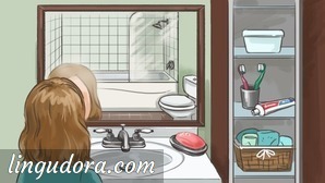 A girl is standing in front of the sink looking at herself in the mirror that also reflects the toilet and a bath tub shower combo. Next to the mirror there is a shelf containing a few hygiene products.